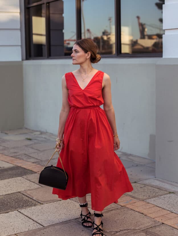 image of a woman in a red midi dress and black sandals walking down the sidewalk