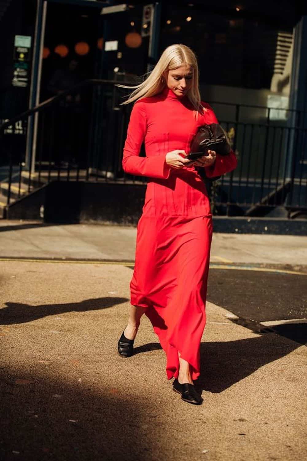 image of a woman wearing a long red dress with long sleeves and black mules walking down the street