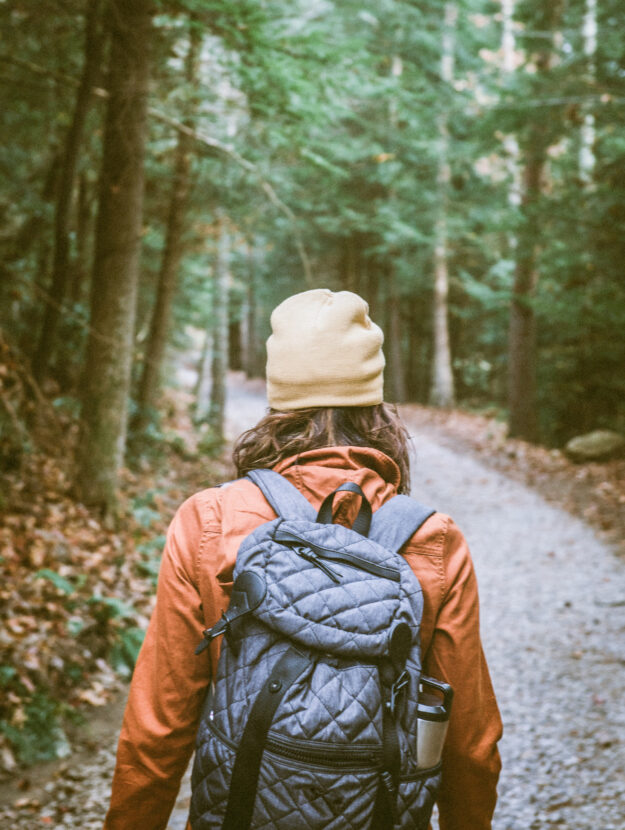 woman walking through a forest with a grey backpack on