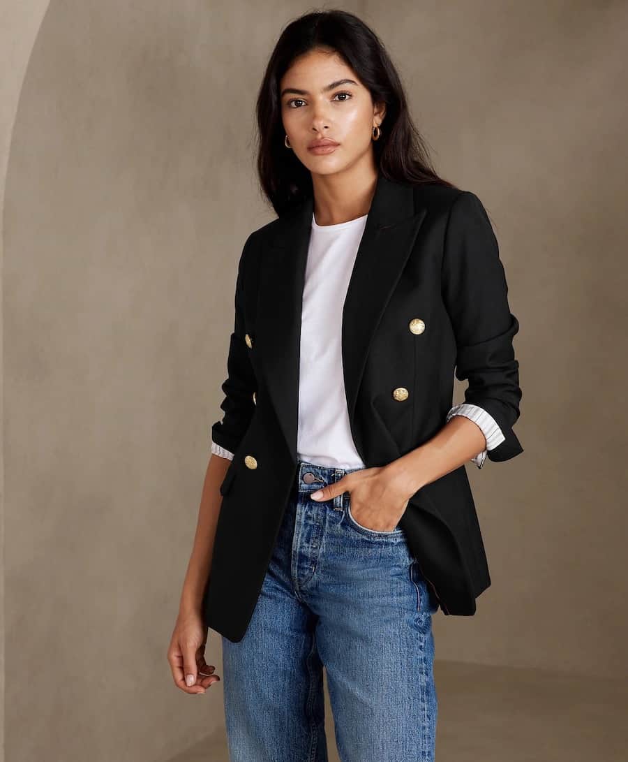 woman wearing a black double-breasted blazer with gold buttons that is a dupe of the Balmain blazer, with a white t-shirt and blue jeans