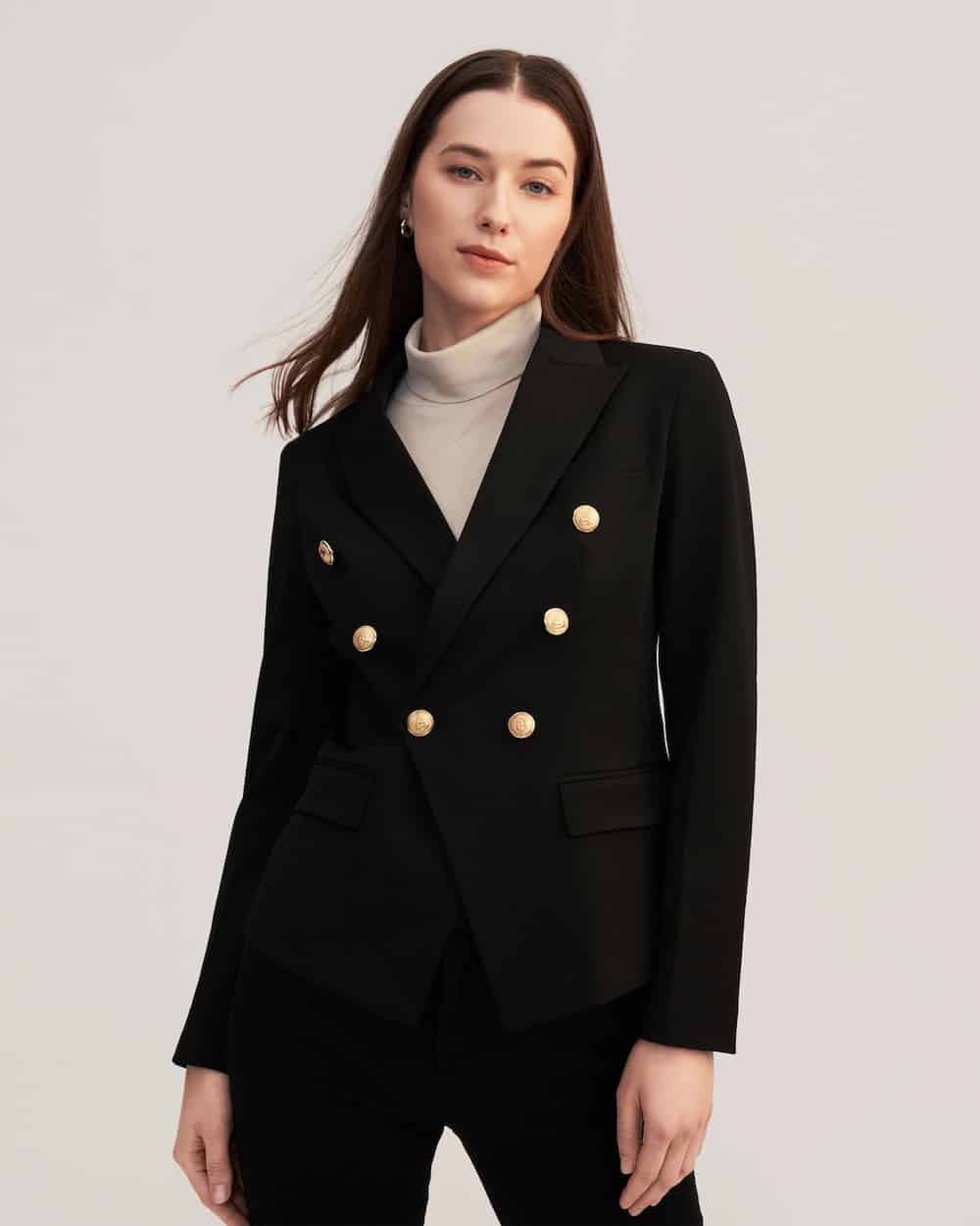 image of a woman wearing a black blazer with gold buttons, and flap pockets over a beige turtleneck