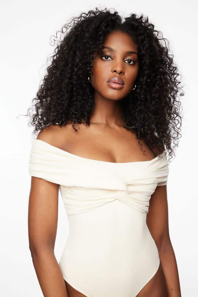 Black woman wearing an ivory off the shoulder ruched bodysuit that is a dupe of the Khaite Cerise bodysuit