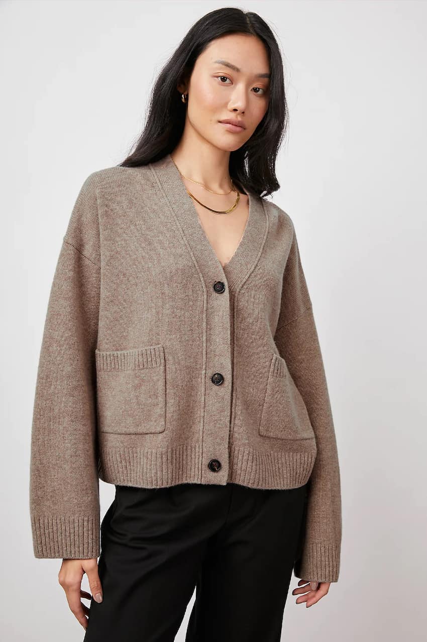 Woman wearing a knit taupe cardigan with three buttons and pockets with a ribbed trim, similar to the Khaite scarlet cardigan