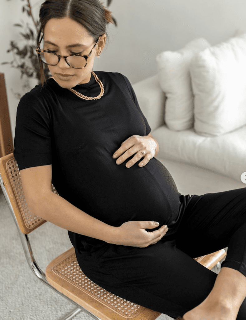 image of a pregnant woman sitting on a chair in a black jumpsuit embracing her belly