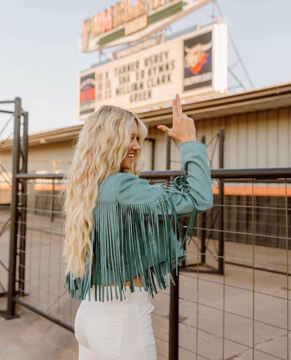 blonde woman wearing a turquoise blue fringe jacket and white jeans 