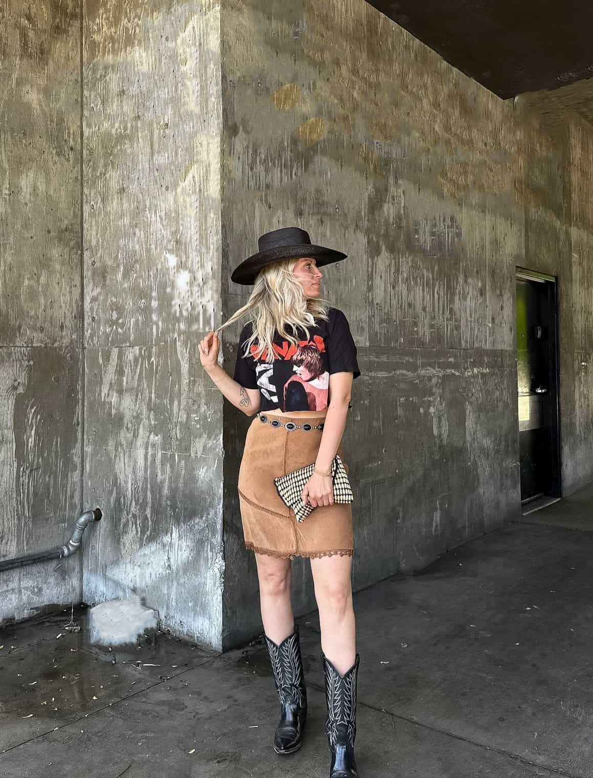 woman wearing a cropped graphic t-shirt, western hat, suede skirt and western belt with cowboy boots for a rodeo outfit