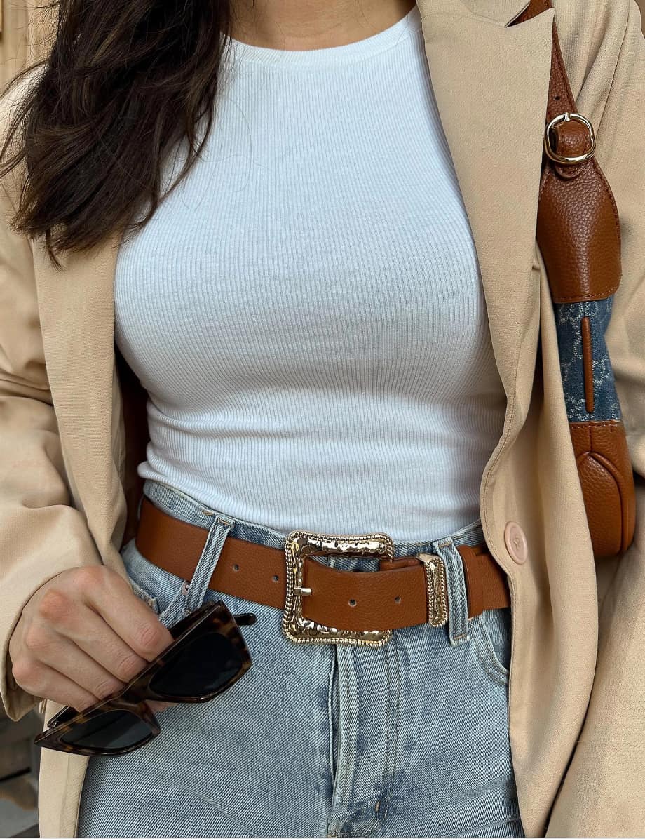 close up of a woman wearing a blazer, white top, western belt, and jeans