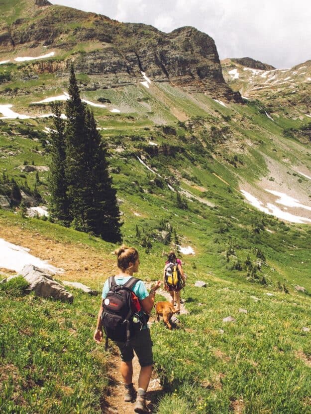 image of two women hiking down a hill path in a green mountain landscape