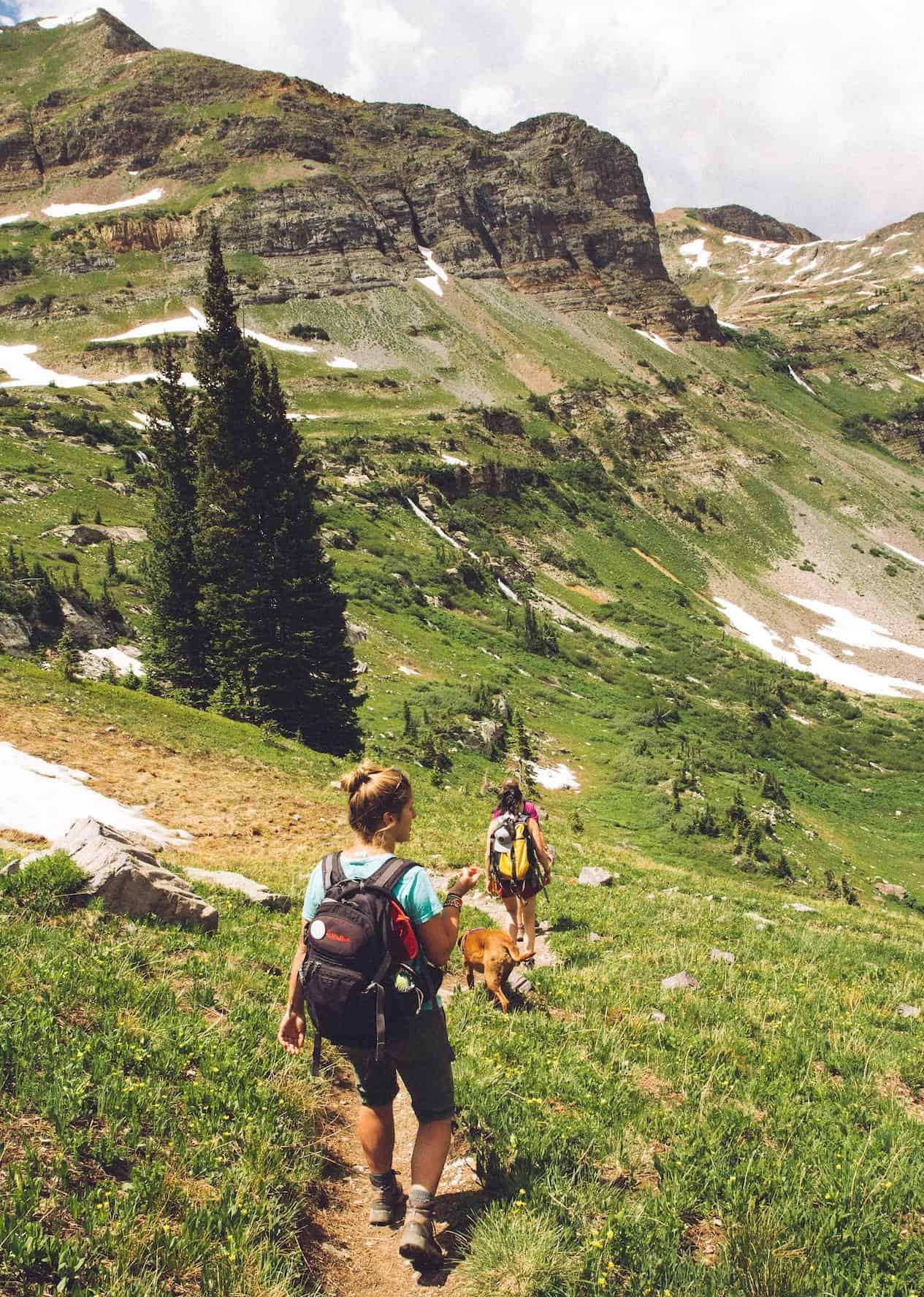 image of two women hiking down a hill path in a green mountain landscape
