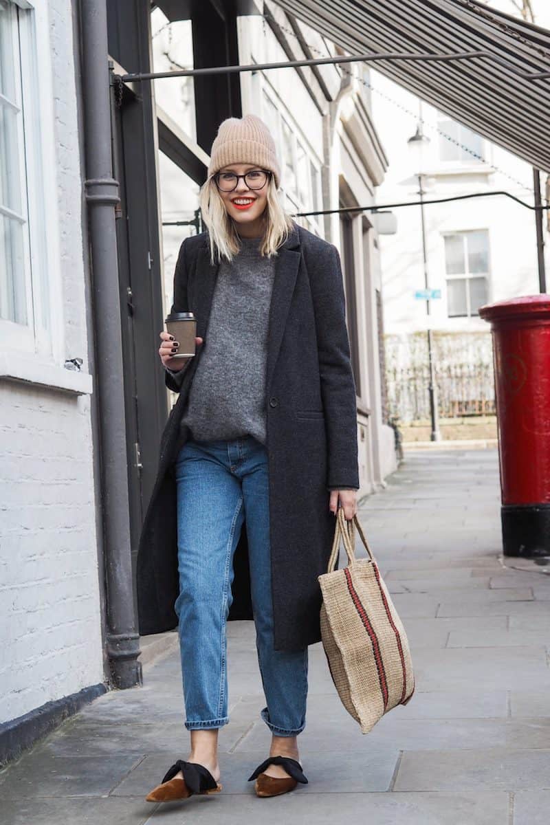 image of a blonde pregnant woman walking down the street wearing jeans, an oversized grey sweater, a wool coat, and a knit toque