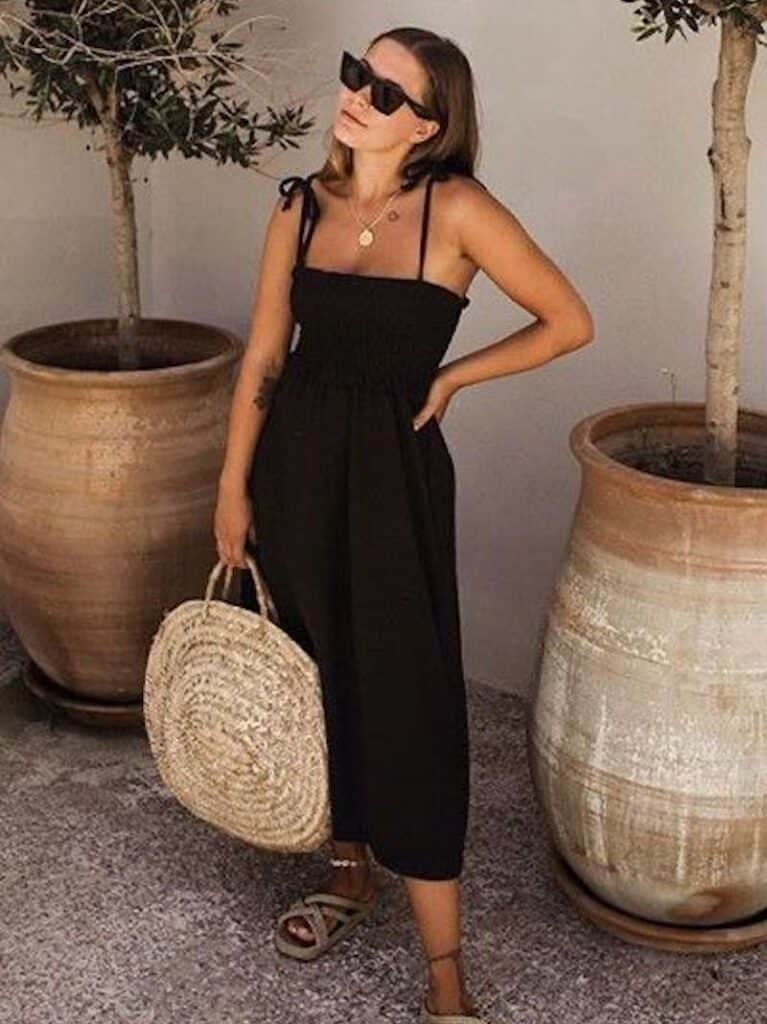 image of a woman wearing a black sun dress holding a large round straw beach tote