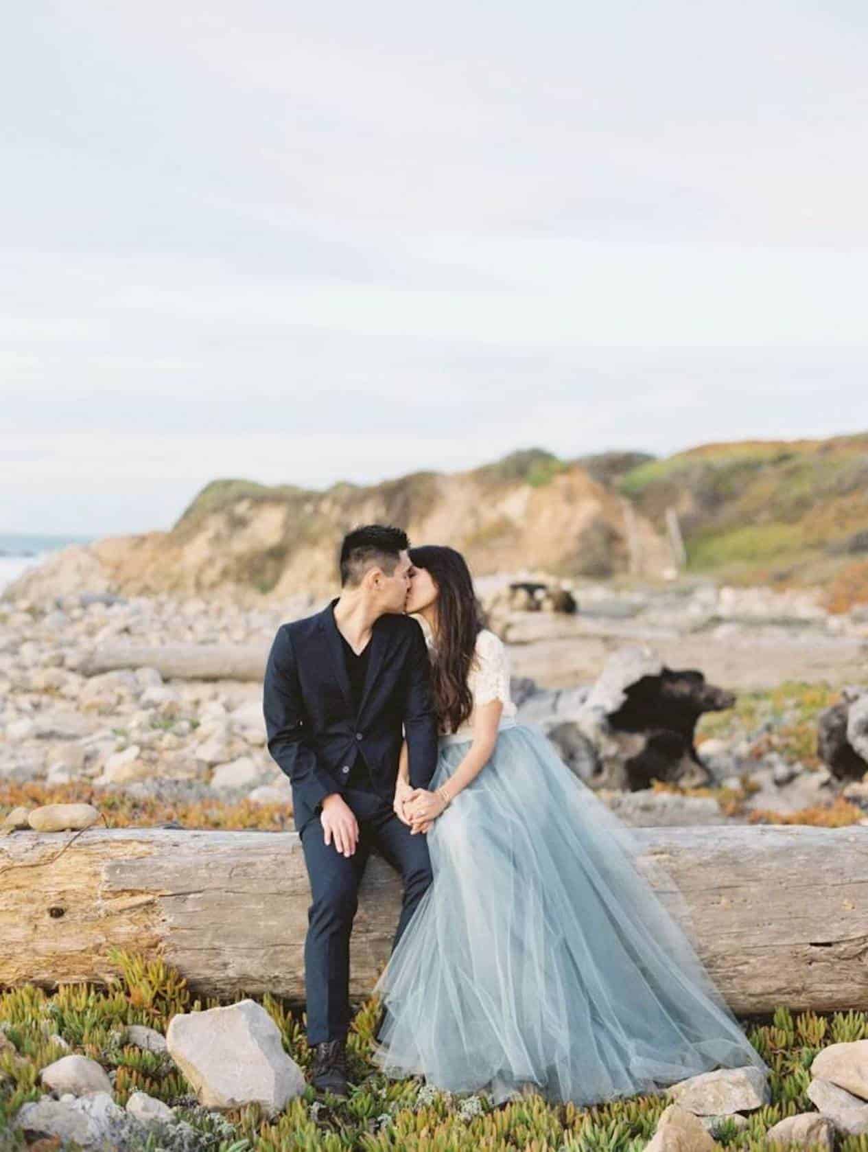 Young man kisses young woman on a fallen tree stump outside. 