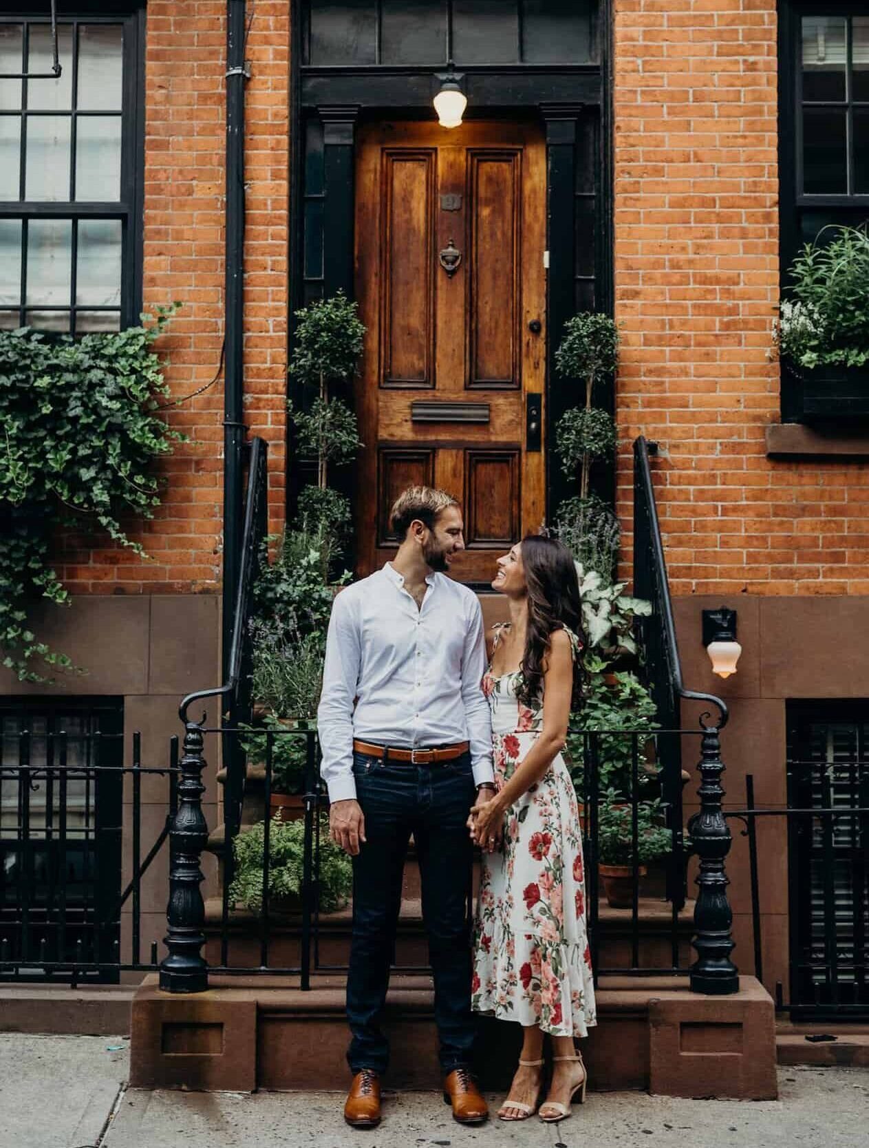 Young man and young woman look at each other lovingly in front of city home.