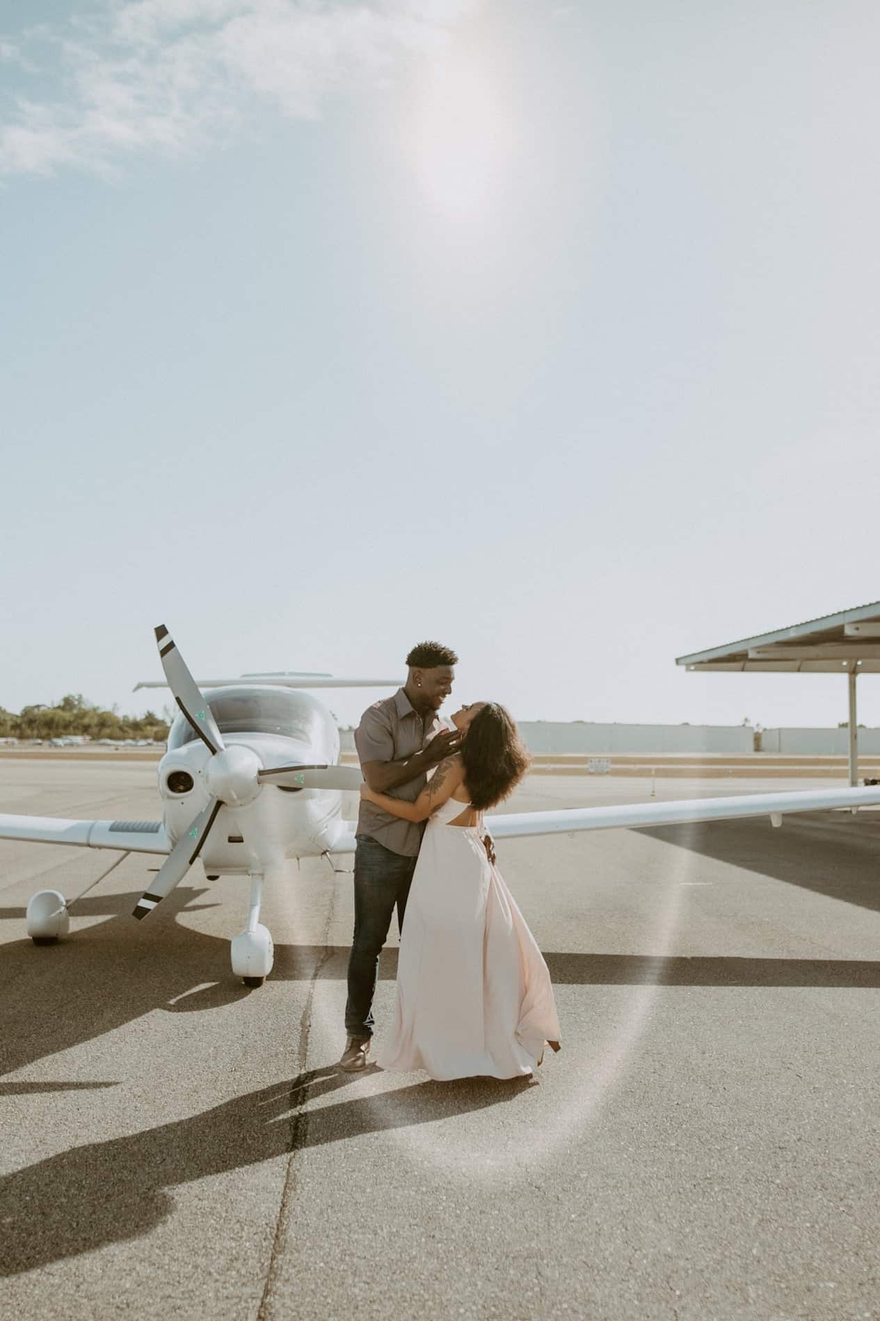 Young man and young woman hug each other in front of small white plane