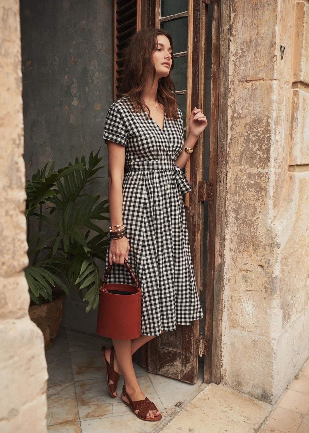 Young woman in a black and white gingham wrap dress poses in an open doorway.