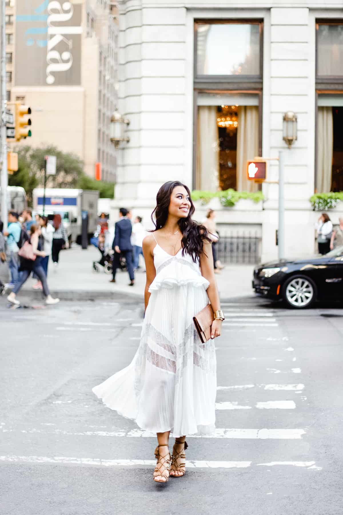 Young woman in white dress walks through a cross walk in the city.