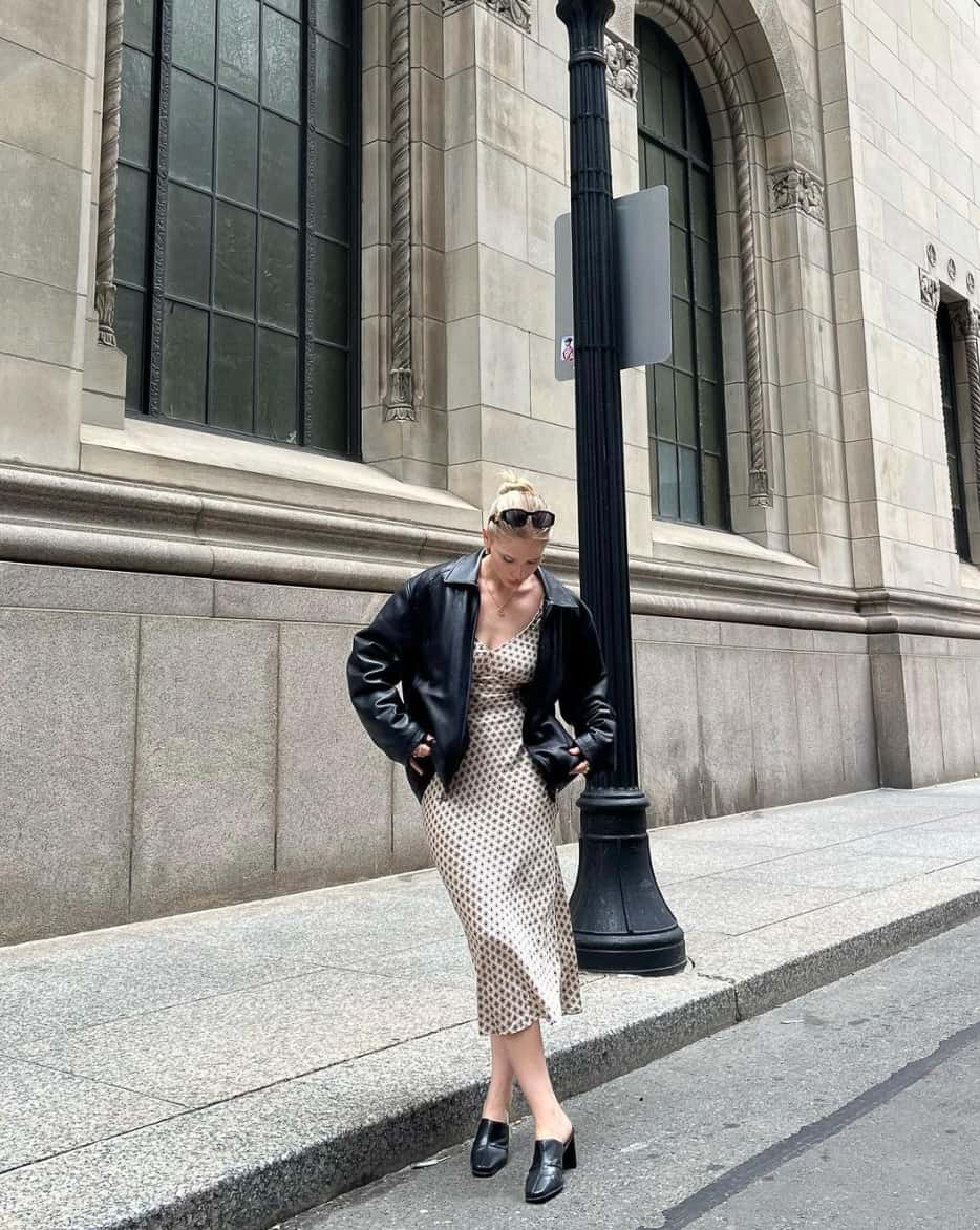 woman wearing an oversized leather bomber jacket with a v-neck slip dress and loafers