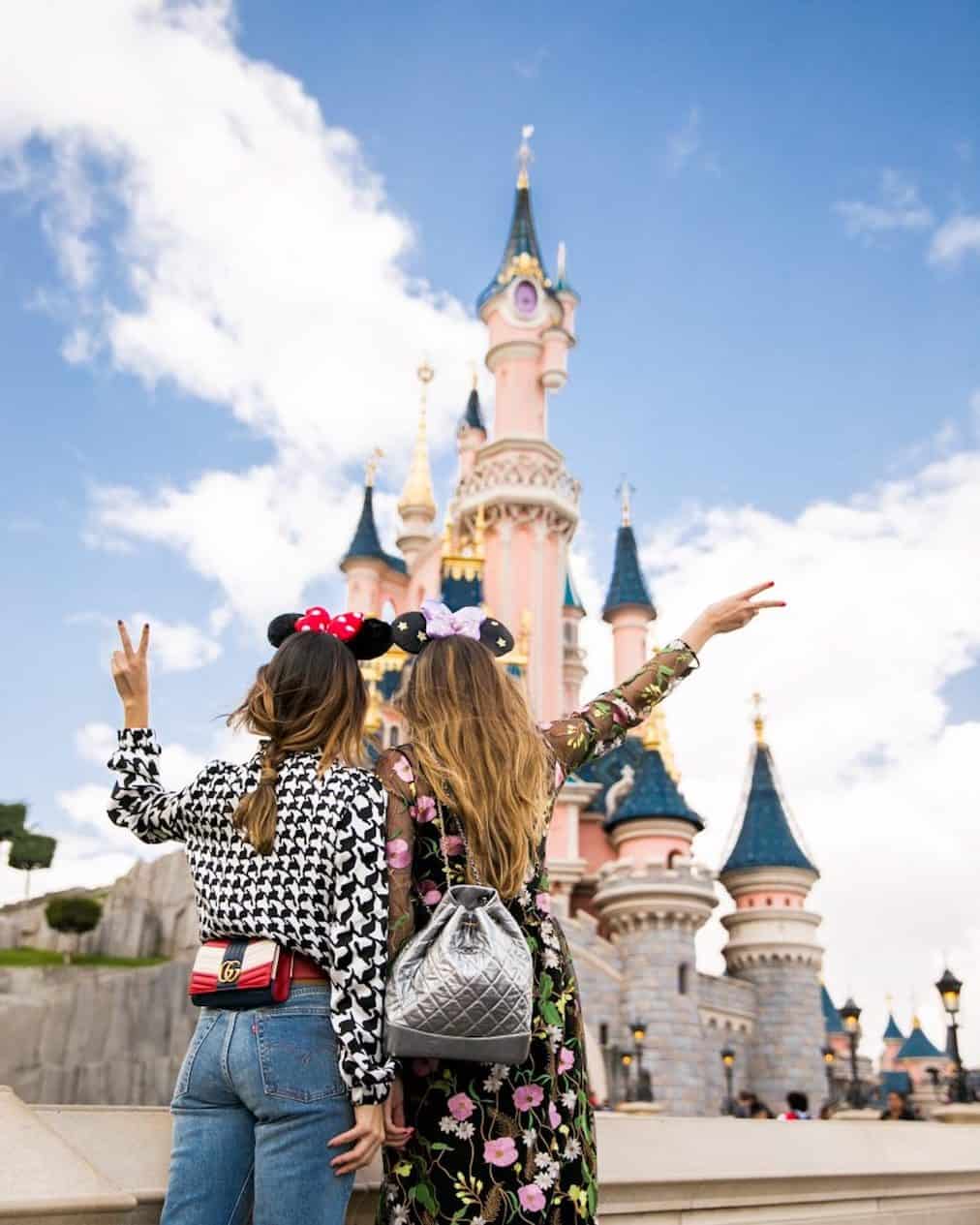 Girls in front of the Disney castle holding up the peace sign and wearing Minnie Mouse ears.