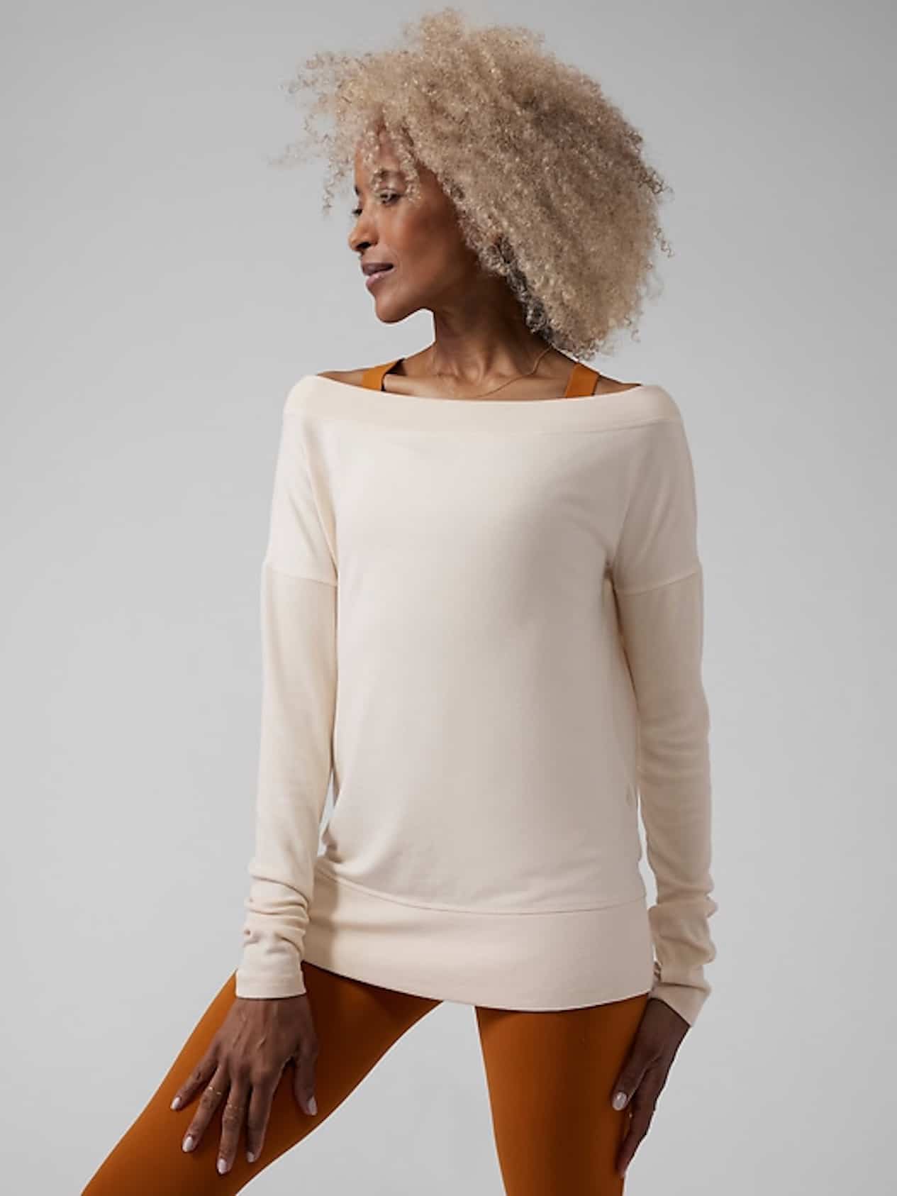 Woman in a white sweater, burnt orange leggings and a burnt orange sports bra