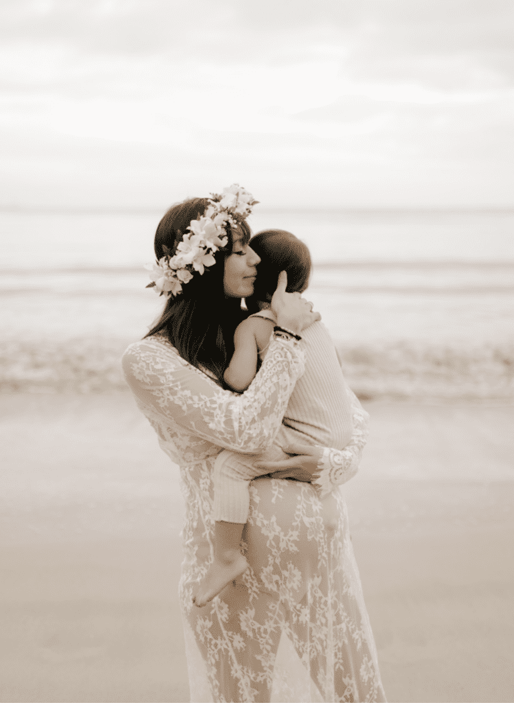 image of a pregnant woman in a sheer lace dress holding a small child in her arms on the beach