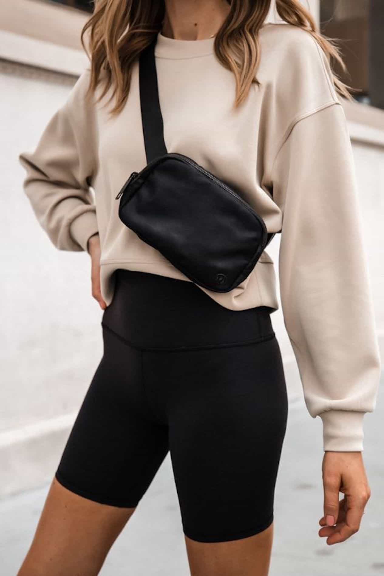 Woman in black biker shorts, cream sweater and black bum bag