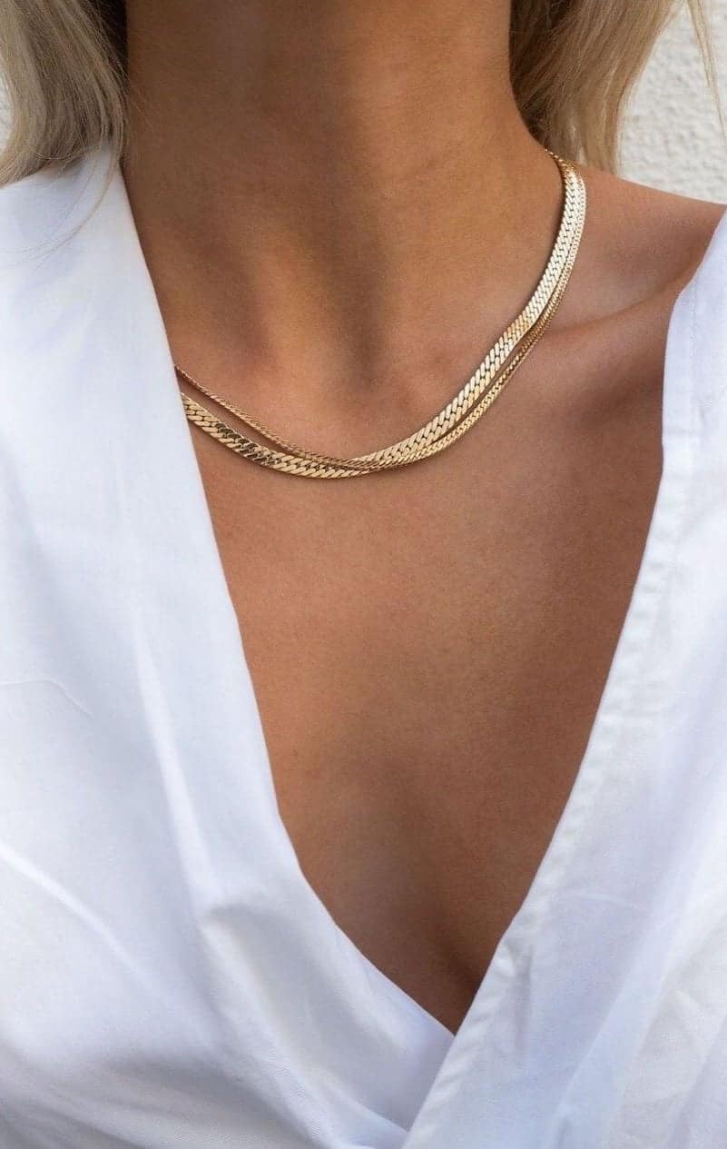 Close up shot of a woman wearing two gold chain necklaces.