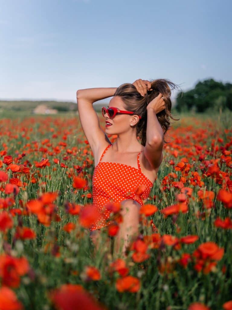 an image of a woman wearing a red polka dot dress and red sunglasses in a poppy field