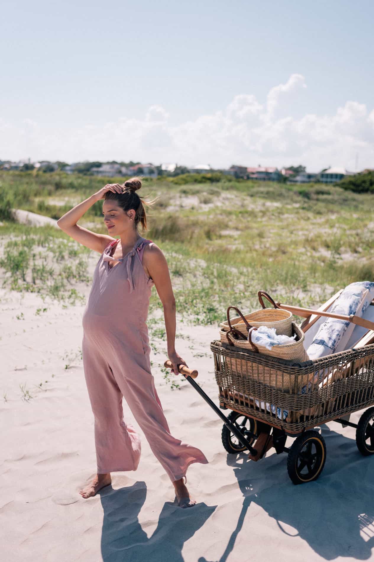 Pregnant woman wearing a pink jumpsuit pulling a wagon onto the beach