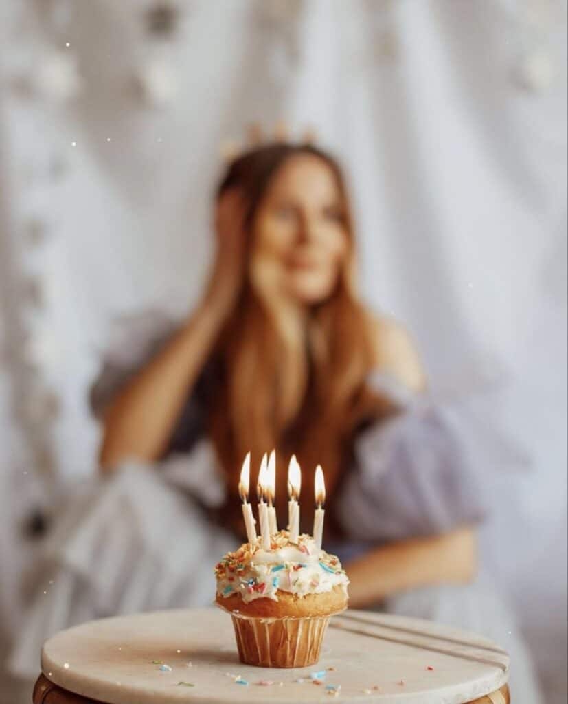 an image of a woman sitting behind a table that is topped with a birthday cupcake with multiple candles