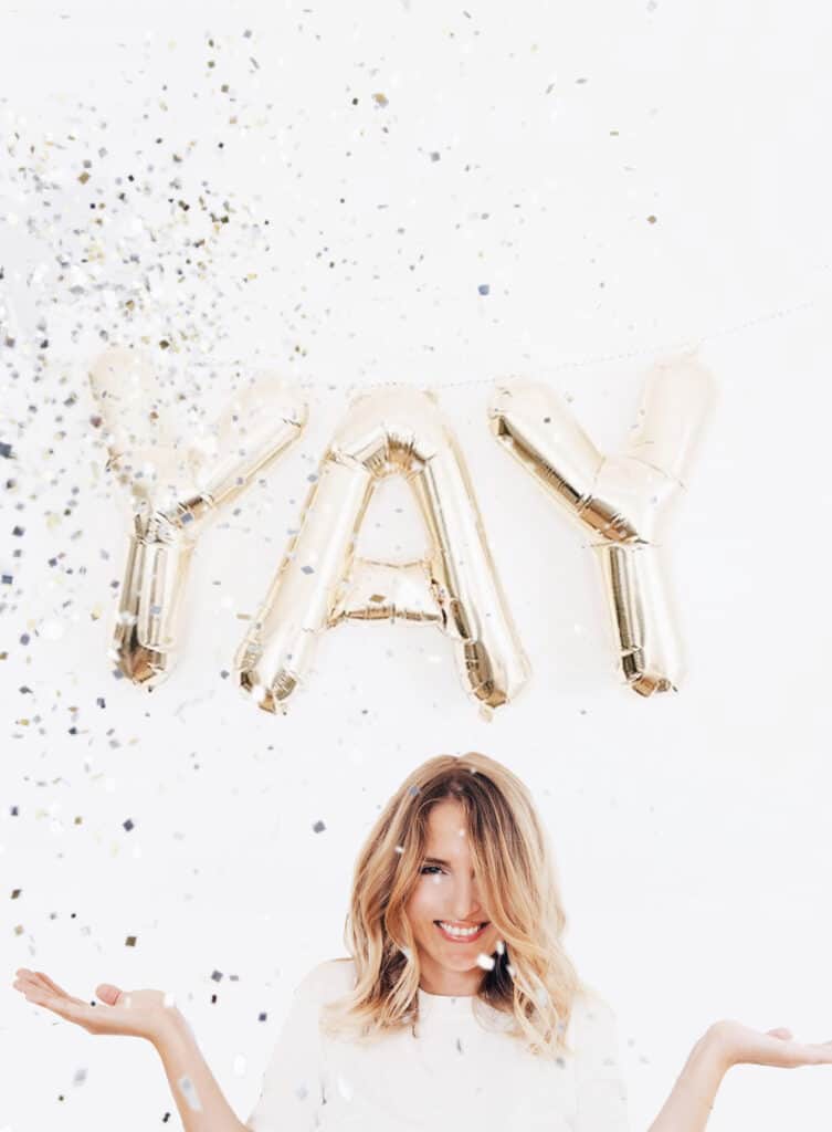 an image of a woman against a white background with silver balloons that spell out the word "yay" and confetti in the air