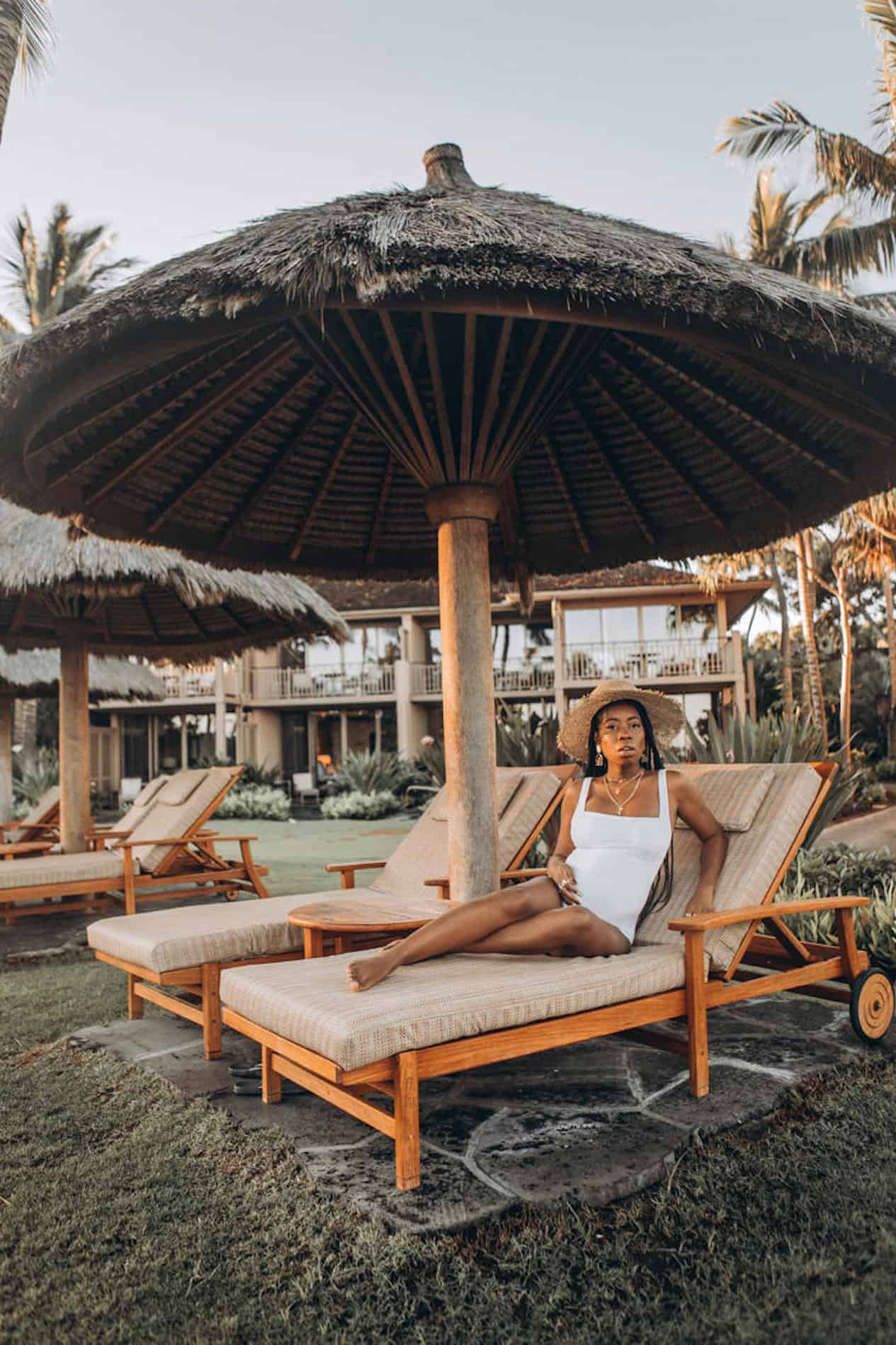 image of a pregnant black woman in a white swimsuit sitting on a lounge chair on a beach with a resort in the background