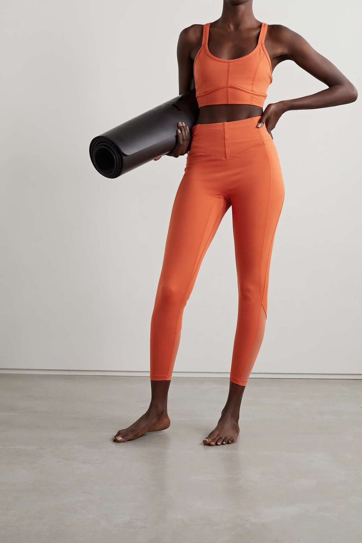 Woman in an orange workout set carrying a foam roller