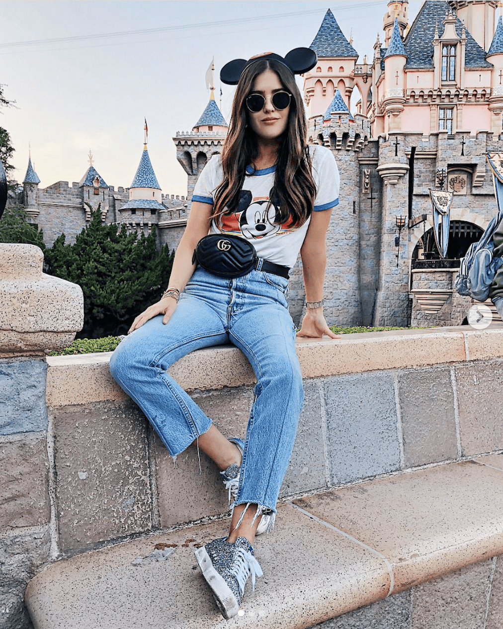Girl at Disney wearing Black Mickey Mouse ears, jeans, silver glitter sneakers, a white Mickey Mouse tee and a black Gucci belt bag.
