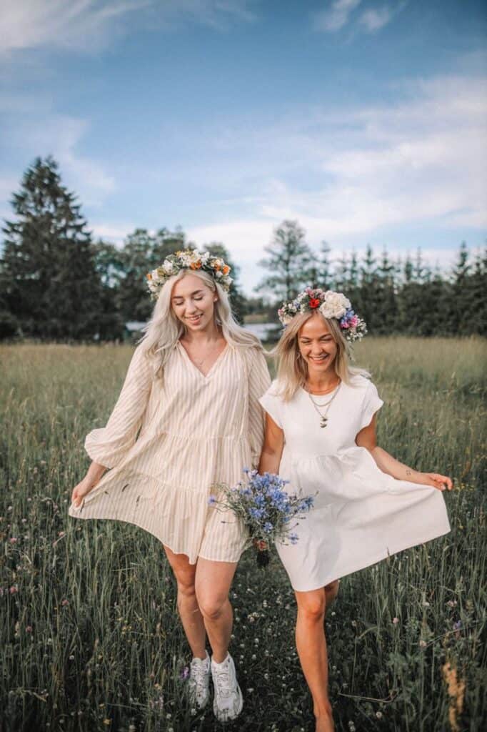an image of two young women walking through a grassy field wearing dresses and flower crowns