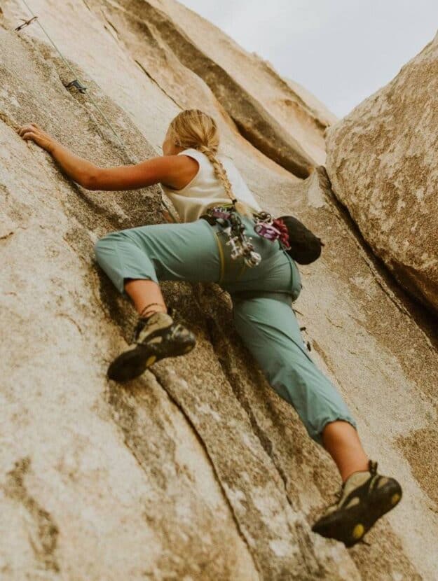 Woman outdoor rock climbing in blue jogger pants and a white tank top.