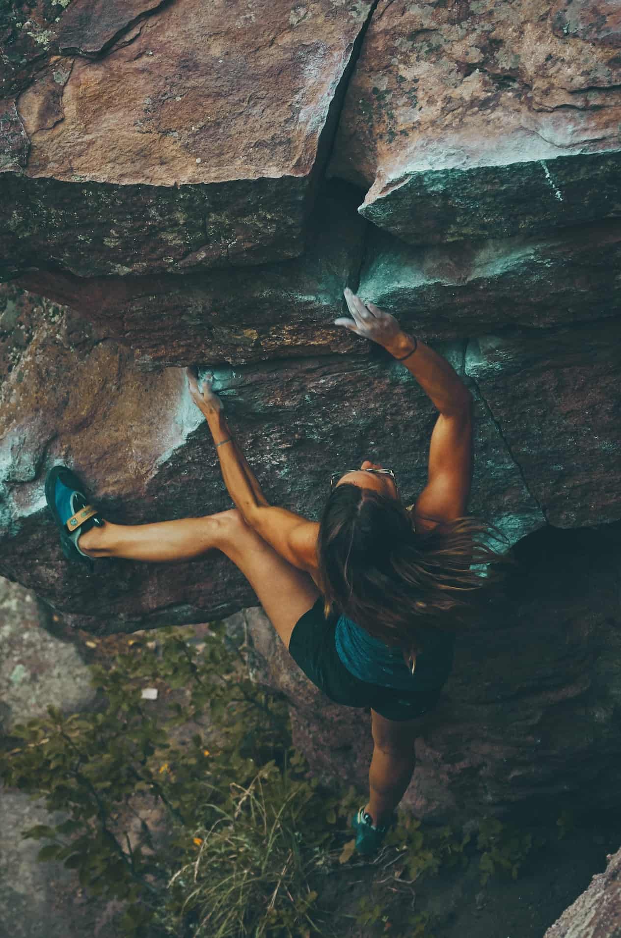 Woman outdoor rock climbing in black shorts and a grey tank top.