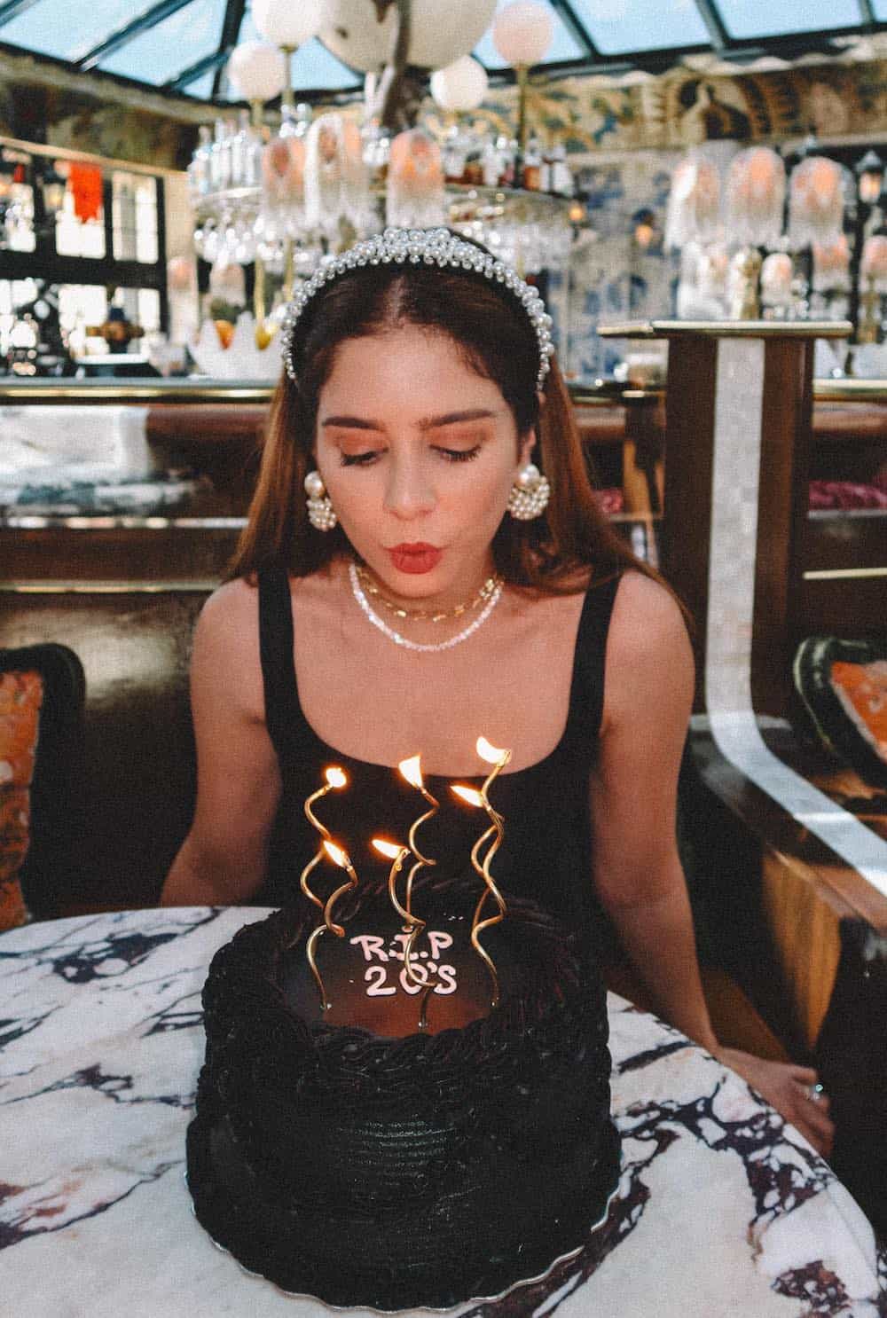 woman blowing out the candles of a cake with "RIP 20's" on it for a birthday photoshoot
