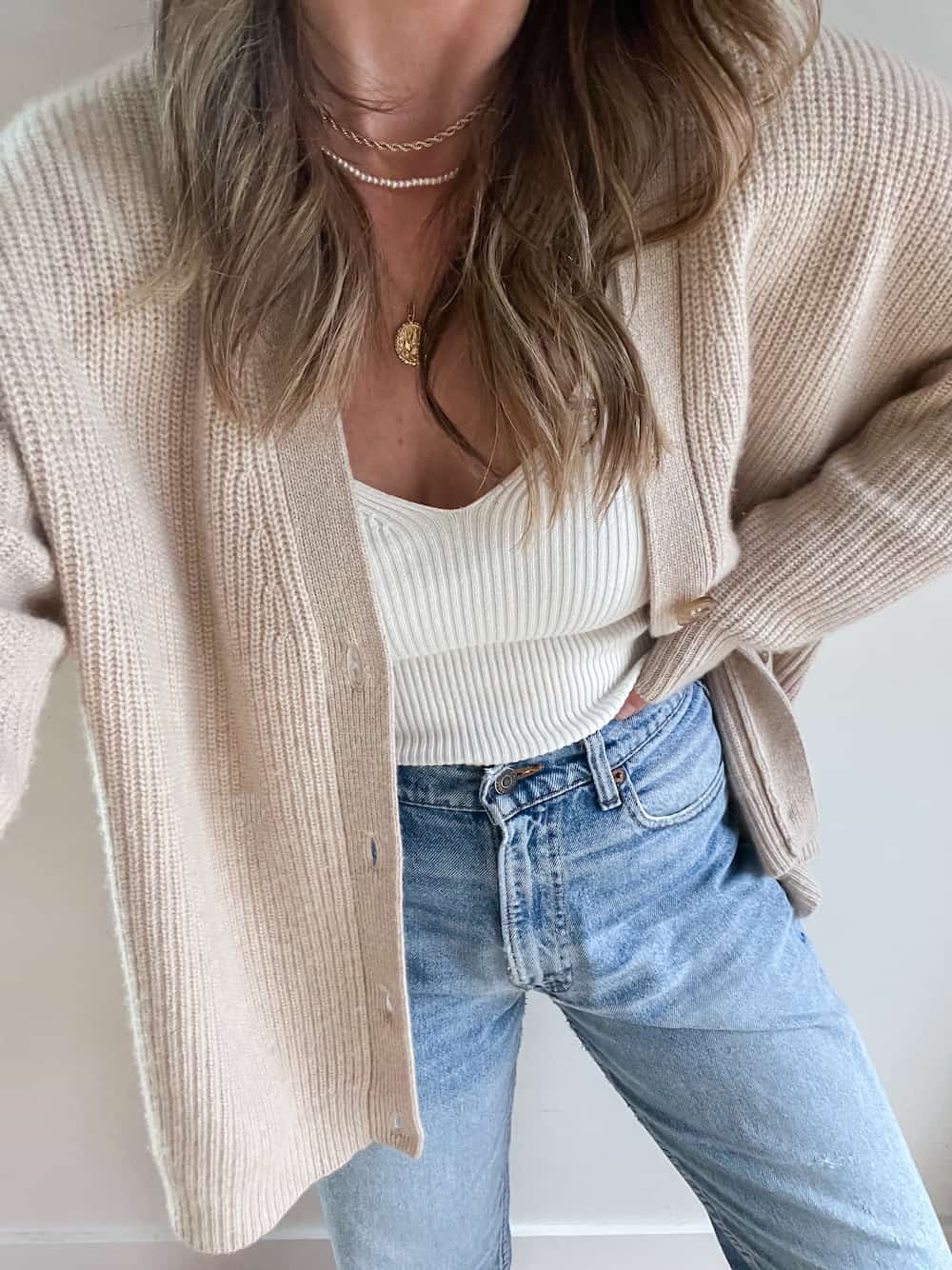 woman wearing a beige cashmere knit oversized cardigan from Jenni Kayne with an ivory ribbed tank top and jeans