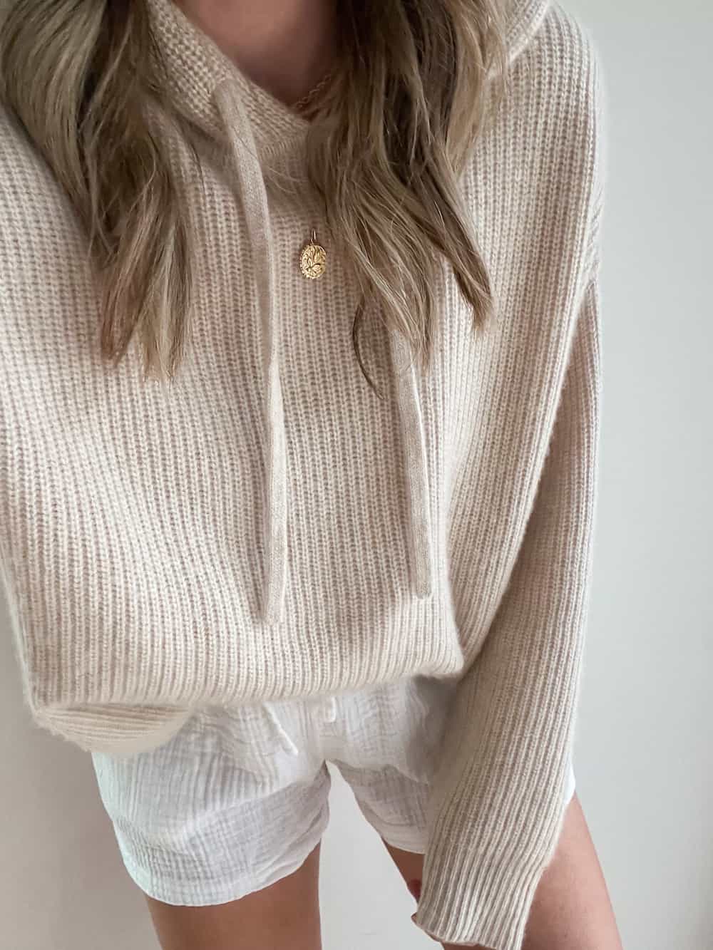 woman wearing a beige cashmere knit hoodie sweater from Jenni Kayne with white crinkle cotton shorts
