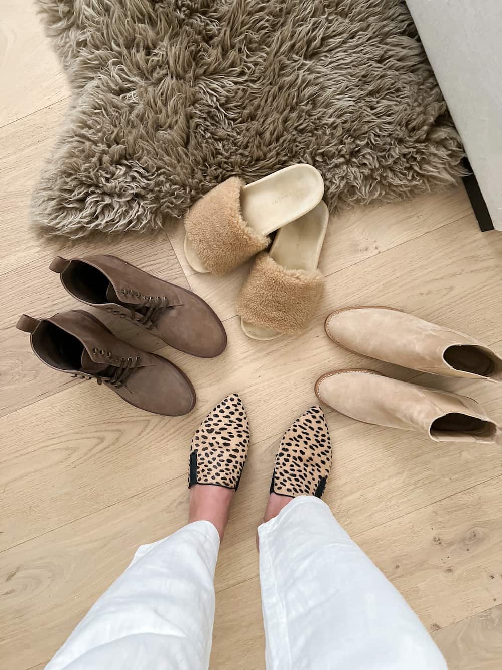 image of an overhead view of four pairs of Jenni Kayne shoes including brown boots, suede tan boots, shearling slides, and leopard mules