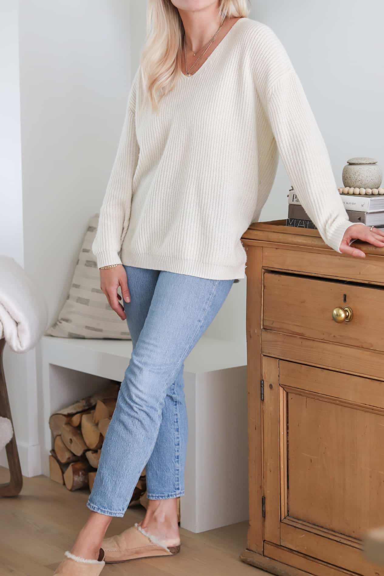 Woman wearing jeans, slippers and a cream colored sweater.