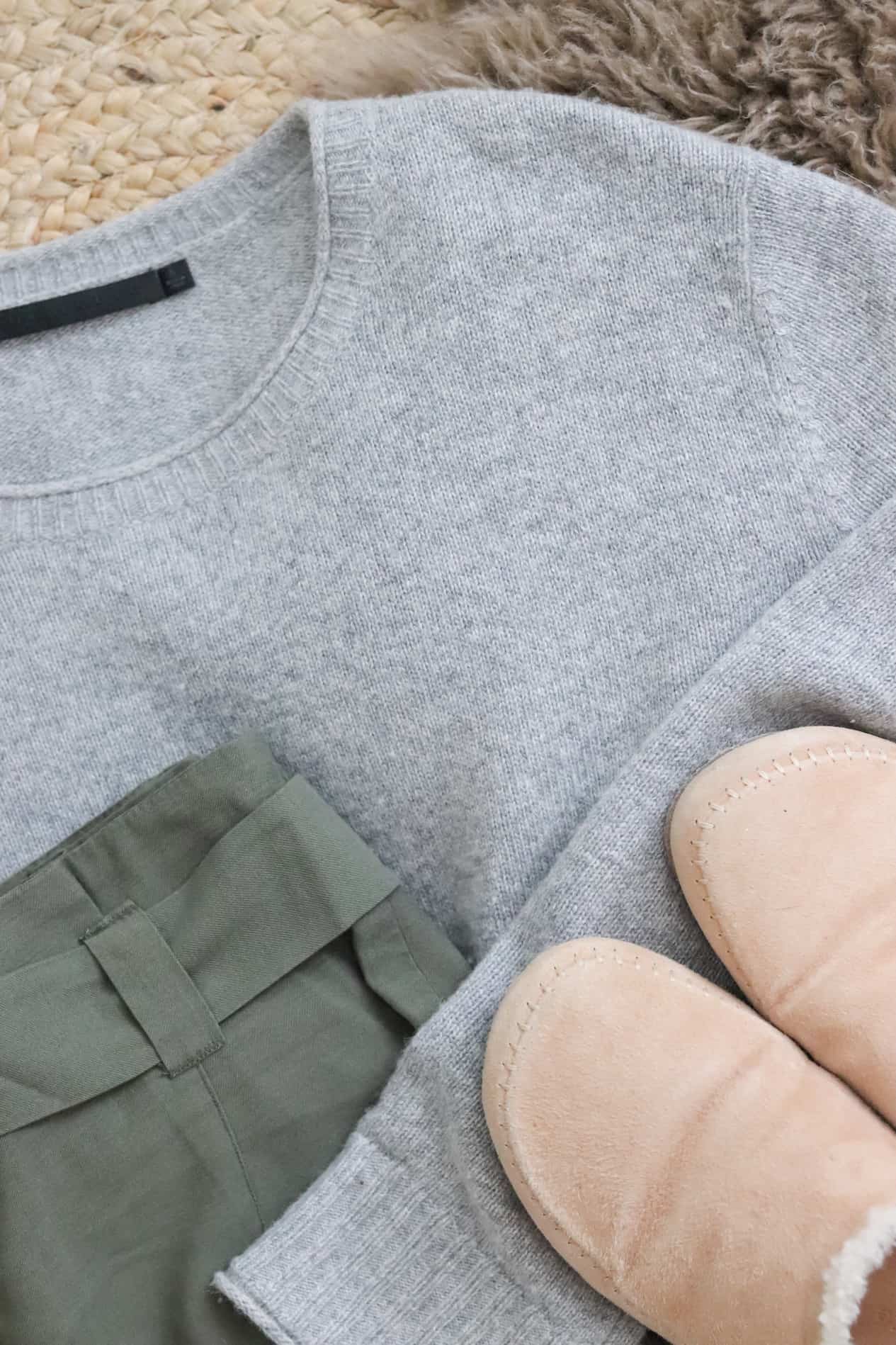 Flat lay. of a grey sweater, green linen pants and cozy slippers.