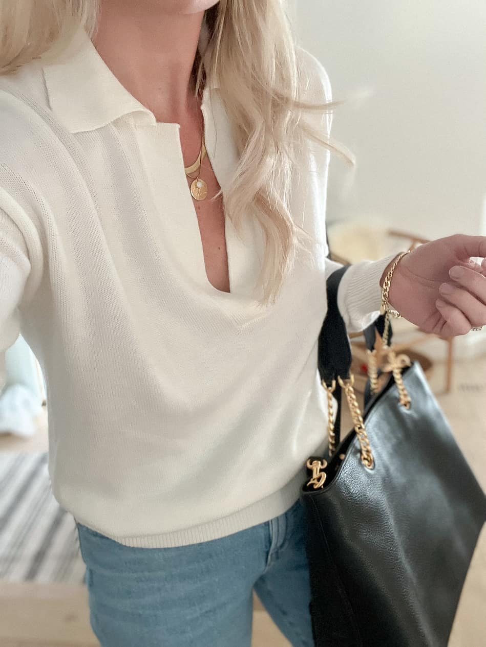 Woman wearing a white sweatshirt, jeans, and a black handbag.