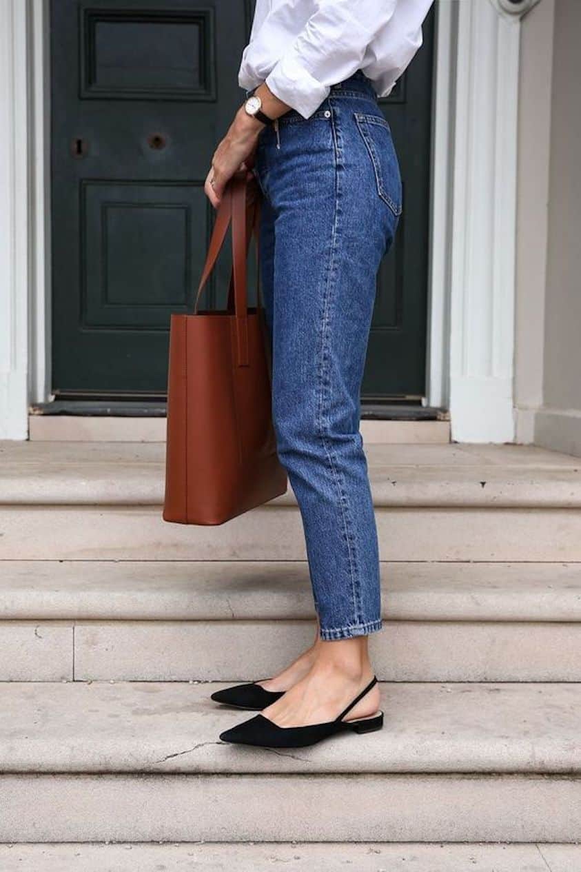 Woman standing on steps wearing jeans, pointed toe black mules and a white button down.