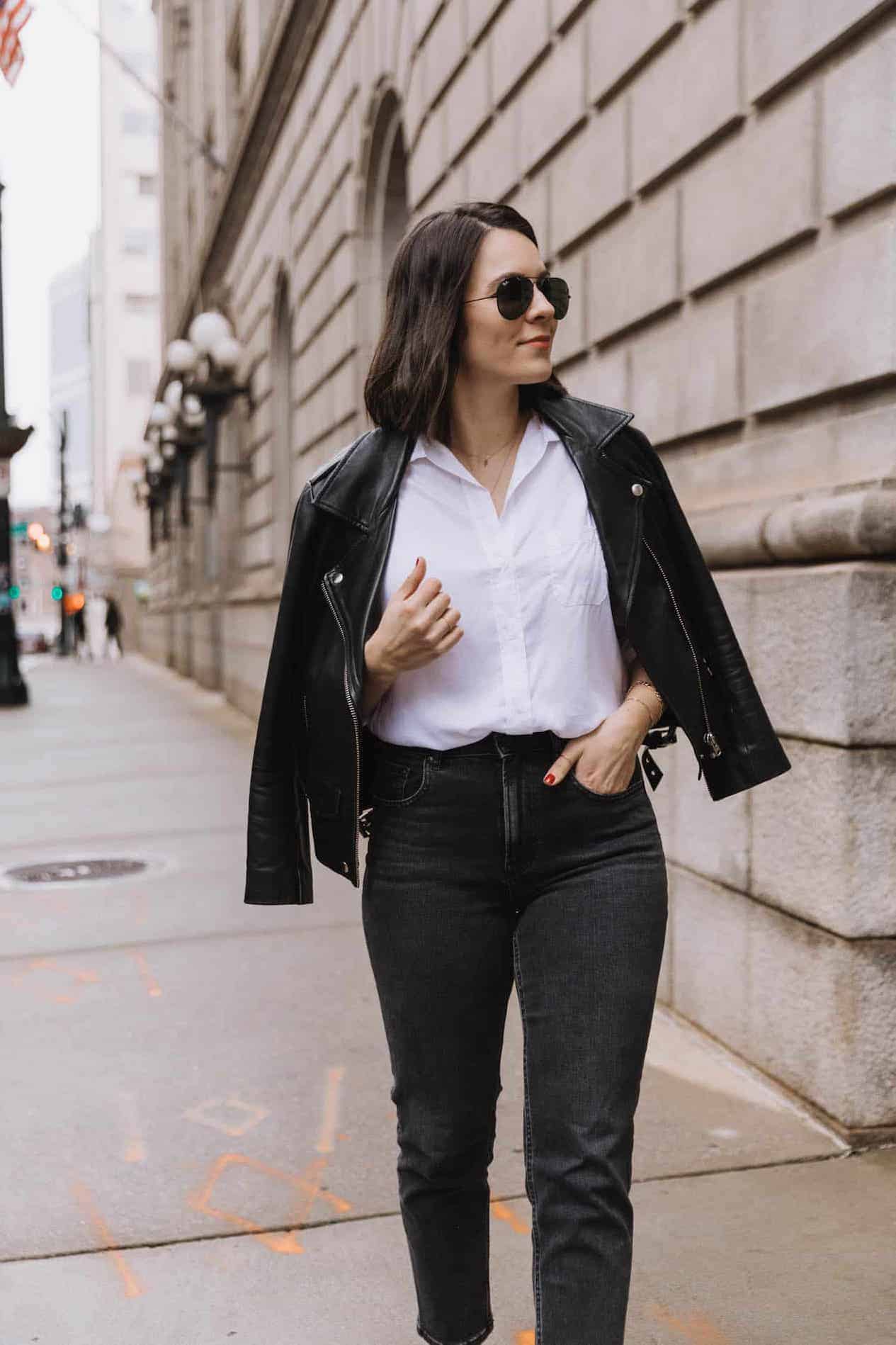 Woman wearing black jeans, a white button down and a black leather jacket.