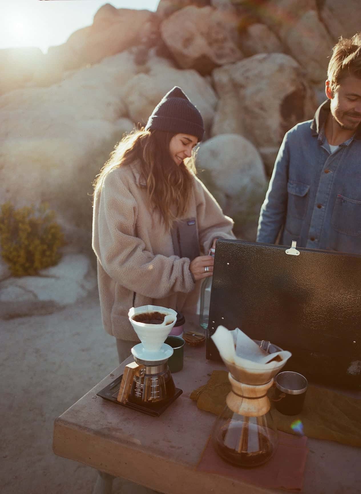 Two people making coffee at a campsite.