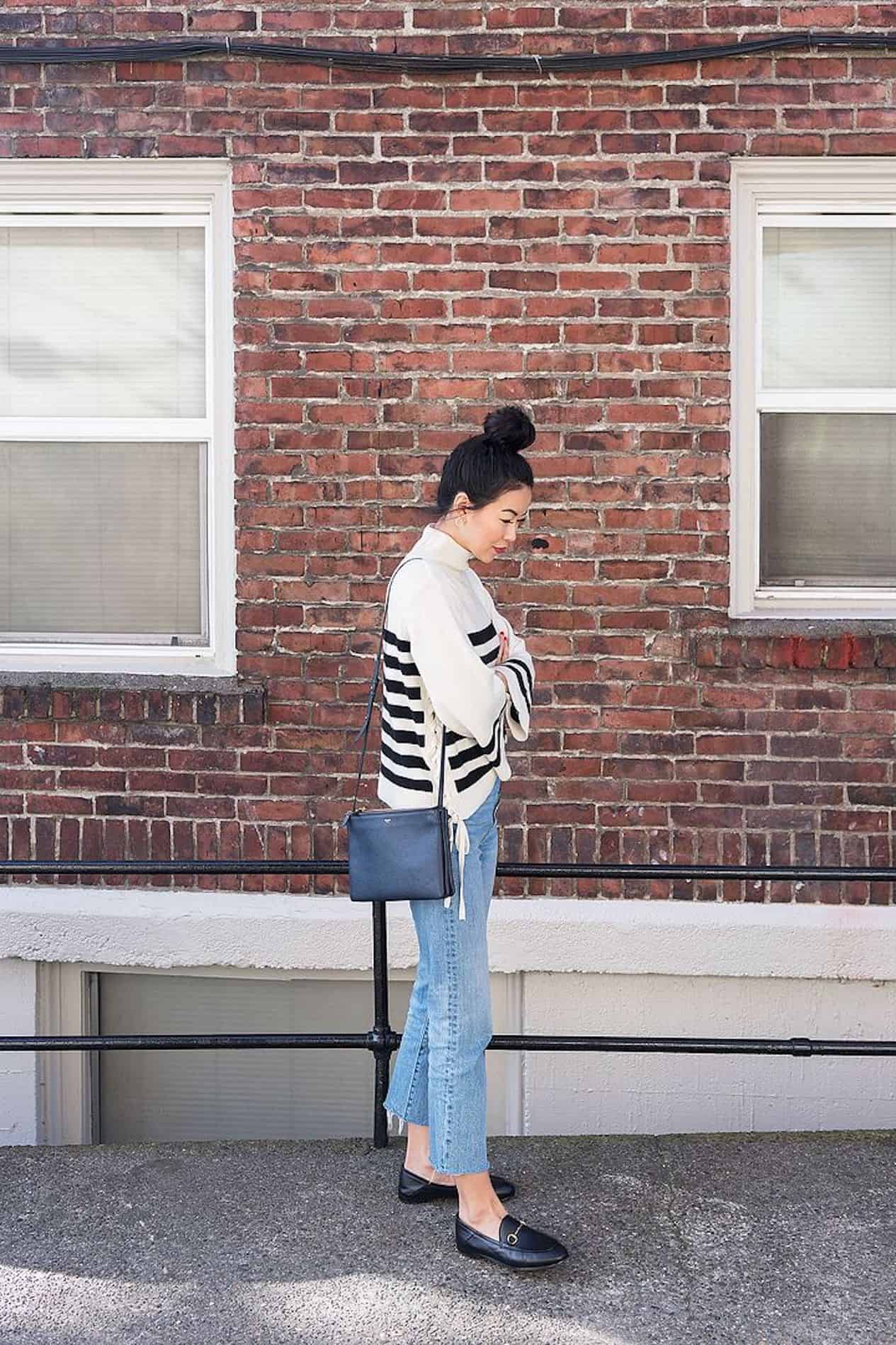 image of a woman standing in front of a brick wall wearing a striped sweater, jeans, and Gucci loafers