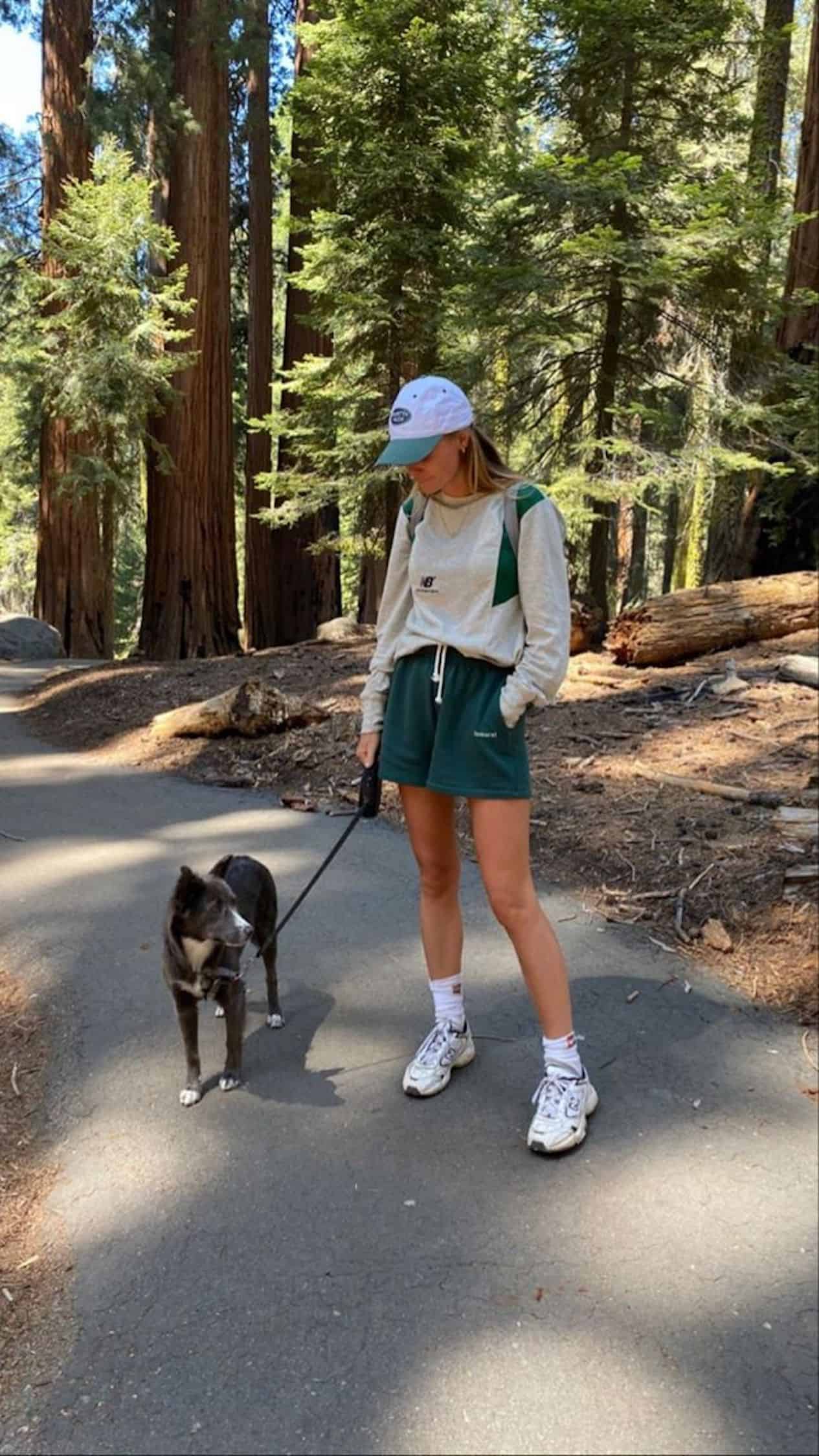 Girl walking her dog on a hike wearing green shorts and a cream sweatshirt.