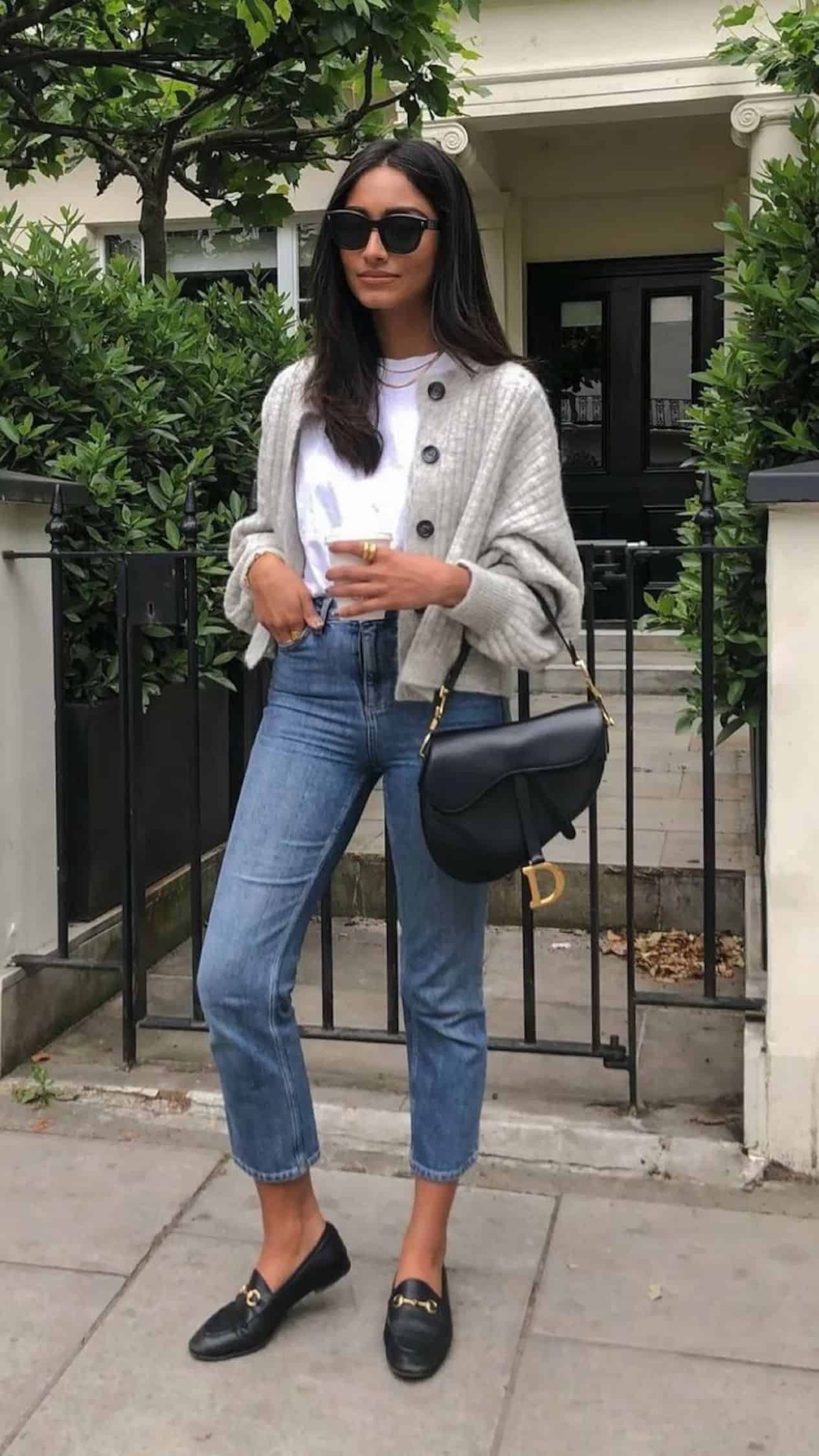 image of a woman with brown hair standing on the sidewalk wearing jeans, a grey cardigan, and Gucci loafers