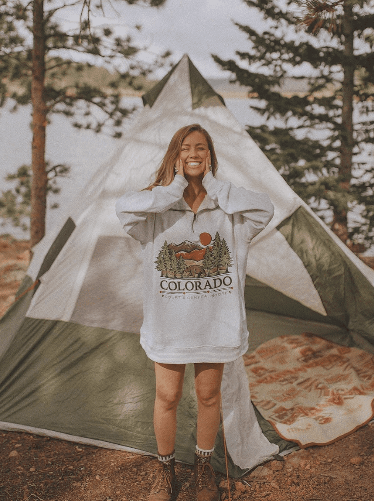 Girl wearing a baggy sweatshirt and hiking boots in front of a tent.